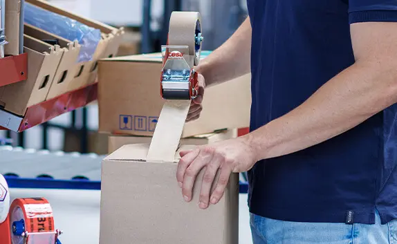 Ein Mitarbeiter von PRODINGER klebt einen Karton mit Papierklebeband zu.