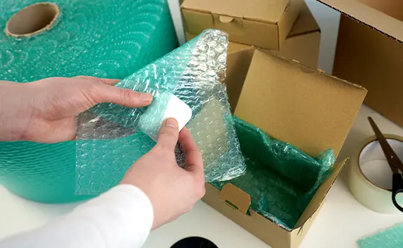 Eine Logistikmitarbeiterin wickelt Earpods in schützende Luftpolsterfolie ein.