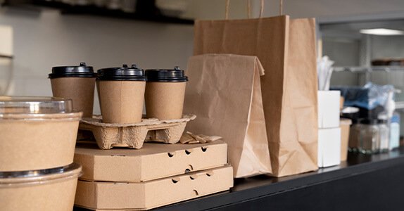 Auf einem Tresen stehen mehrere Lebensmittelverpackungen wie Becher, Pizzakartons und Papiertaschen.