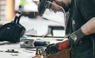 Ein Arbeiter mit Schutzkleidung schneidet mit einem Winkelschleifer ein Metallstück.