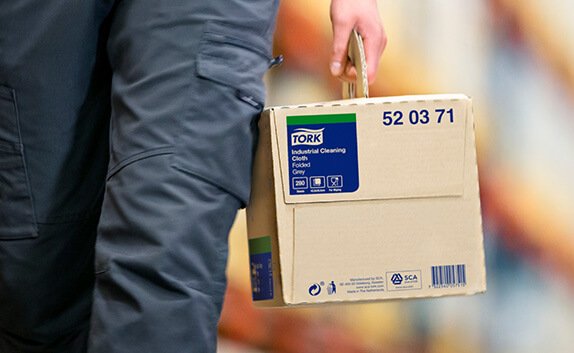 Eine Person trägt einen Karton mit Hygiene-Produkte von Tork.