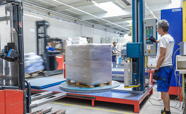 PRODINGER Mitarbeiter bedient Stretchmaschine in der Logistik, im Hintergrund steht weitere Verpackungstechnik