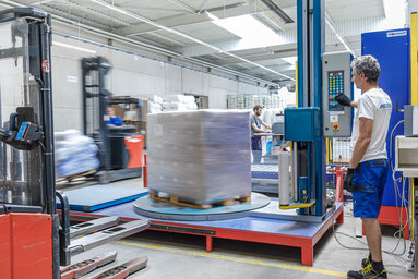 PRODINGER Mitarbeiter bedient Stretchmaschine in der Logistik, im Hintergrund steht weitere Verpackungstechnik