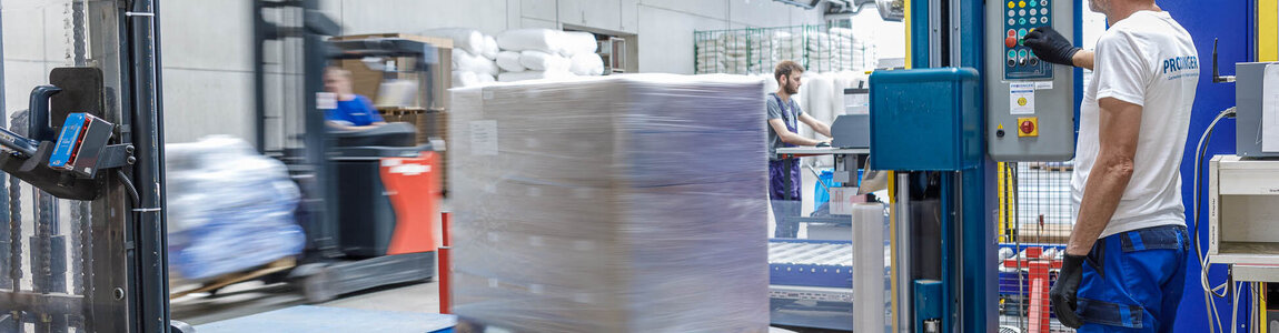 PRODINGER Mitarbeiter bedient Stretchmaschine in der Logistik, im Hintergrund steht weitere Verpackungstechnik