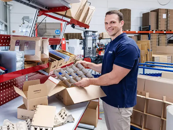 Ein Mitarbeiter im Logistikzentrum verpackt Produkte in Kartonagen.