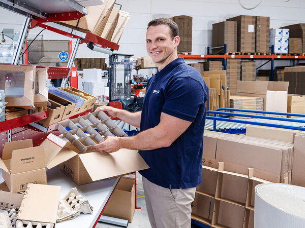 Ein Mitarbeiter im Logistikzentrum verpackt Produkte in Kartonagen.