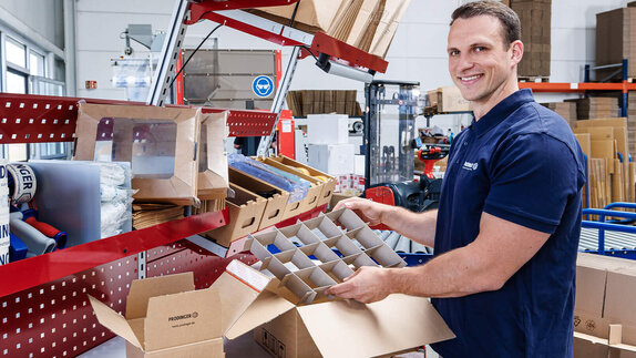 Ein Mitarbeiter im Logistikzentrum verpackt Produkte in Kartonagen.