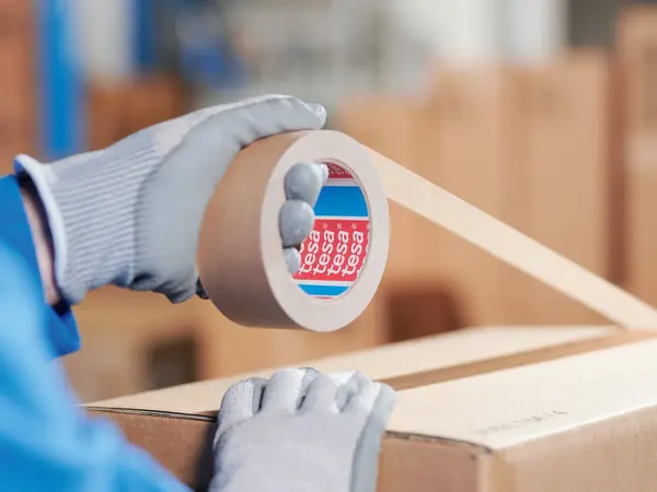 Ein Logistikmitarbeiter verklebt einen Karton mit Papierklebeband.