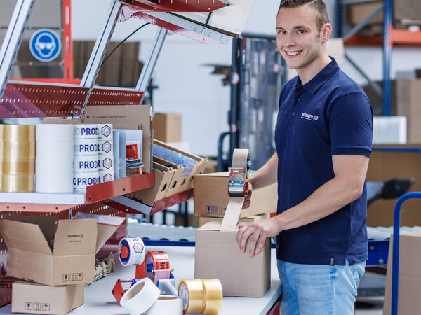 Mitarbeiter im Logistikzentrum klebt einen Karton mit einem Paketabroller zu.