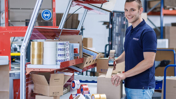 Mitarbeiter im Logistikzentrum klebt einen Karton mit einem Paketabroller zu.