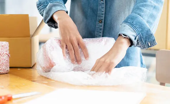 Ein Logistikmitarbeiter im E-Commerce-Bereich verpackt Produkte mit Luftpolsterfolie geschützt in Kartons.