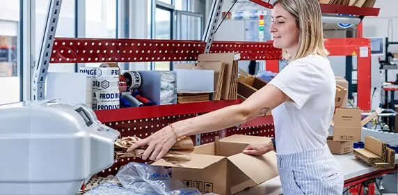 Logistikmitarbeiterin packt ein Paket und schützt das Produkt mit Polstermaterial