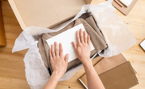 Eine Frau packt einen Pulli in einen Karton, der als Maxibrief versendet werden kann.