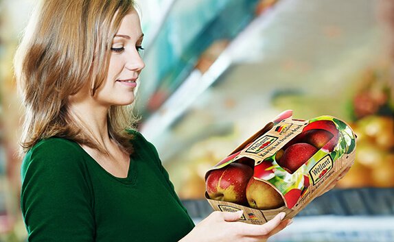 Eine Frau steht im Supermarkt und betrachtet eine Obstverpackung mit Äpfeln.