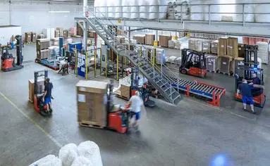 In einem Logistikzentrum fahren mehrere Gabelstabler mit Paletten.