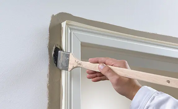 Ein Mann streicht eine Wand, an der eine Tür mit Kreppband geschützt ist, damit sie keine Farbe abbekommt.