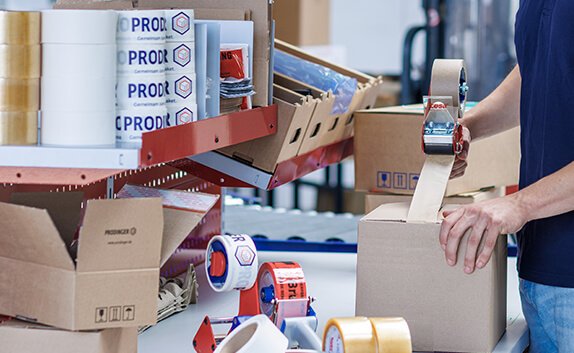 Ein Logistikmitarbeiter verklebt einen Karton mit Paketband