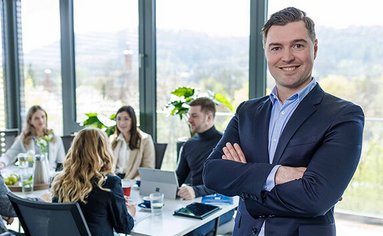 Ein Verpackungsberater steht in einem Besprechungsraum im Vordergrund. Im Hintergrund sitzen Kunden und besprechen ein Verpackungskonzept.
