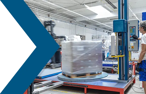 In einem Warenlager wickelt ein Logistikmitarbeiter eine Palette mit Paketen mit einer Stretchmaschine in Stretchfolien ein.