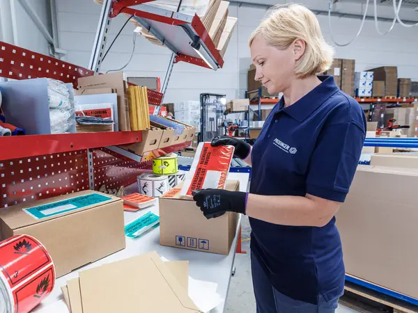 Eine Mitarbeiterin klebt eine Begleitpapiertasche für Versandpapiere auf ein Paket.