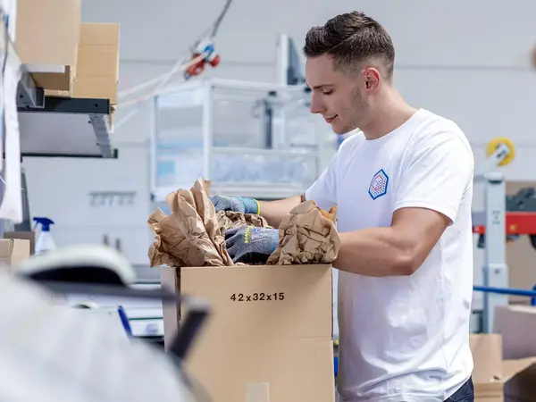 Zwei Logistikmitarbeiter*innen verpacken Produkte in einen Karton.
