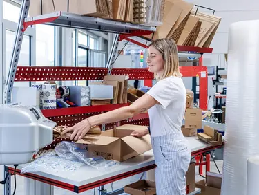 PaperBubble erzeugt Papierpolster, die in die Kartonage an einem Packtisch mit diversen Schutz- und Polstermaterialien, wie z. B. Luftpolsterfolie, zum Schutz des Produkt beigelegt werden.
