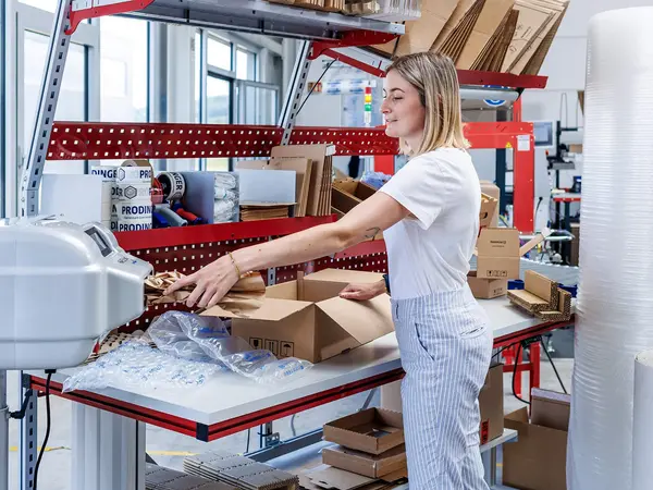 PaperBubble erzeugt Papierpolster, die in die Kartonage an einem Packtisch mit diversen Schutz- und Polstermaterialien, wie z. B. Luftpolsterfolie, zum Schutz des Produkt beigelegt werden.