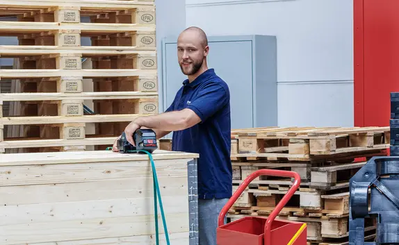 Lager-Mitarbeiter sichert Waren auf einer Palette mit einem Umreifungsband.