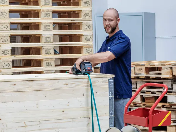 Lager-Mitarbeiter sichert Waren auf einer Palette mit einem Umreifungsband.
