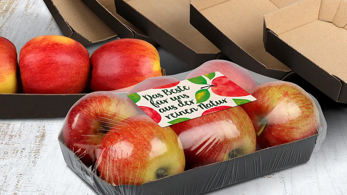 Äpfel in einer Kartonschale, die mit recycelter Folie verschlossen ist.