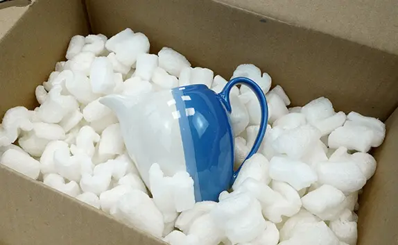 In einem Karton liegt ein durch Verpackungschips geschütztes Milchkännchen.