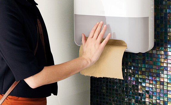 Eine Frau betätigt Rollenhandtuch-Spender von Tork in einer Toilette.