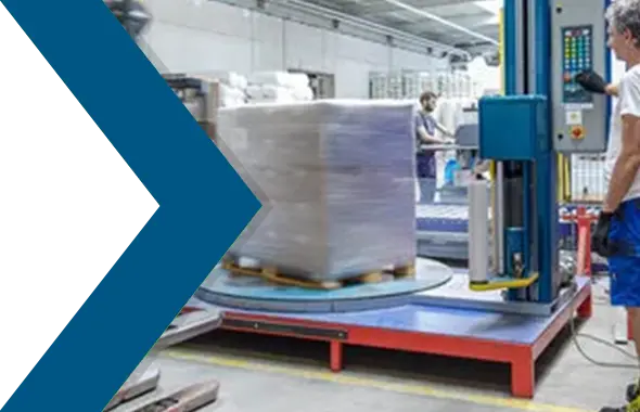 Ein Logistikmitarbeiter bedient eine Stretchmaschine, die eine Palette mit Paketen einwickelt.