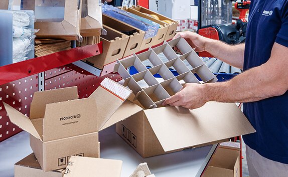 Ein Logistikmitarbeiter steckt ein Gefache in einen Karton.