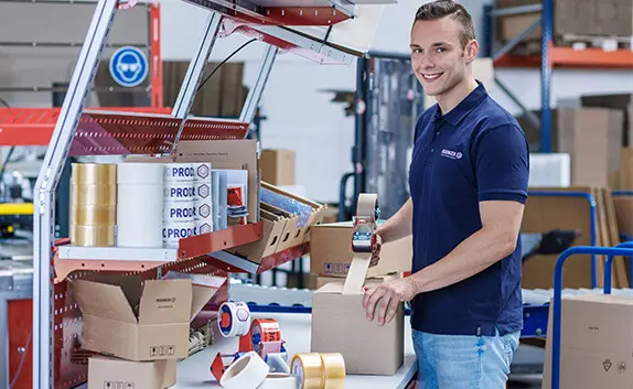 Logistikmitarbeiter verschliesst einen Faltkarton mit einem Packband