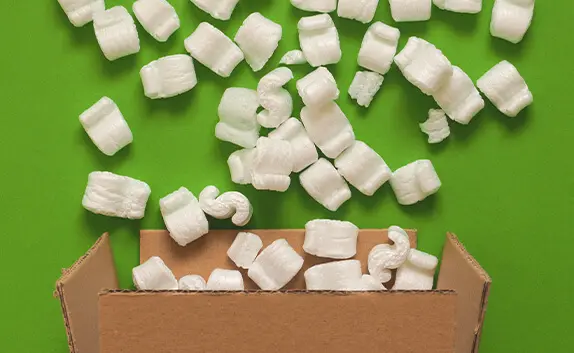 Aus einem geöffneten Karton fallen Verpackungschips heraus.