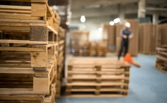 In einem Lager stapeln sich EPLA-Paletten, ein Mitarbeiter fährt mit einem Hubwagen Paletten.