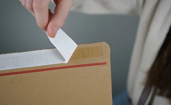 Eine Frau zieht den Selbstklebeverschluss eines Kartons ab, um das Paket zu verschließen.