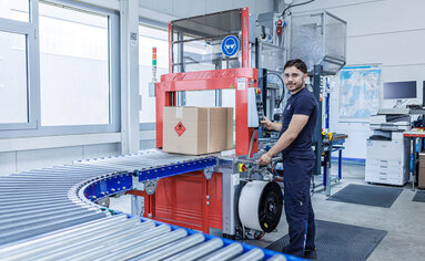 PRODINGER Mitarbeiter bedient vollautomatische Umreifungsmaschine an Paketversandstraße