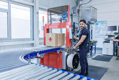 PRODINGER Mitarbeiter bedient vollautomatische Umreifungsmaschine an Paketversandstraße