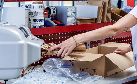 Logistikmitarbeiterin polstert ein Paket mit Papier aus.