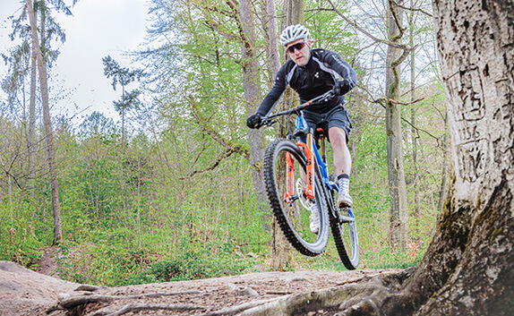 Radfahrer springt im Wald mit seinem Mountainbike über einen kleinen Hügel.